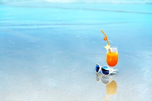 Glass of orange juice and sunglasses on tropical beach
