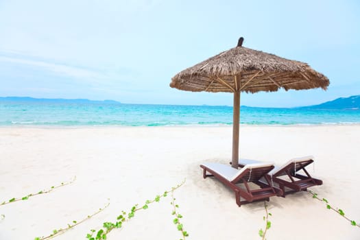 Sandy tropical beach with deck chairs in sunny day