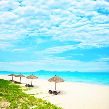 Sandy tropical beach with deck chairs in sunny day