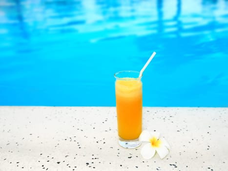 Glass of juice on the edge of swimming pool