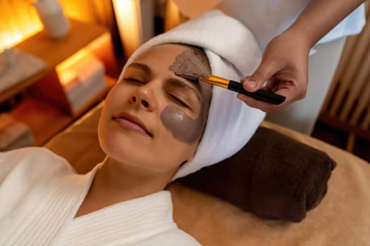 Serene ambiance of spa salon, woman customer indulges in rejuvenating with charcoal face cream massage with warm lighting candle. Facial skin treatment and beauty care concept. Quiescent