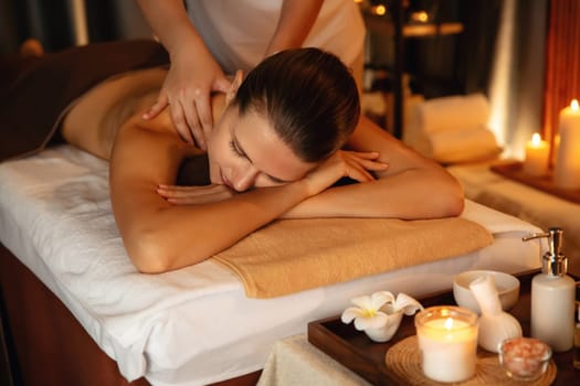 Caucasian woman customer enjoying relaxing anti-stress spa massage and pampering with beauty skin recreation leisure in warm candle lighting ambient salon spa at luxury resort or hotel. Quiescent