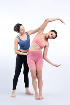 Asian woman in sportswear doing yoga exercise in standing pose with her trainer or yoga buddy. Healthy body care and meditation yoga lifestyle in full shot on isolated background. Vigorous