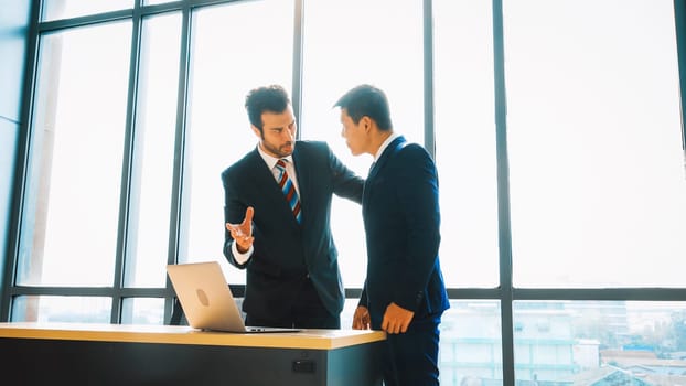 Two business people talk project strategy at office meeting room. Businessman discuss project planning with colleague at modern workplace while having conversation and advice on financial report. Jivy