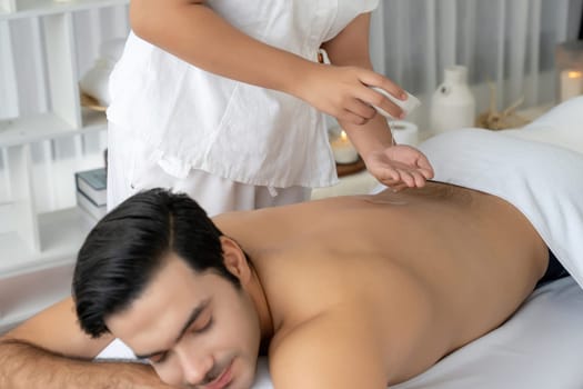 Caucasian man customer enjoying relaxing anti-stress spa massage and pampering with beauty skin recreation leisure in day light ambient salon spa at luxury resort or hotel. Quiescent