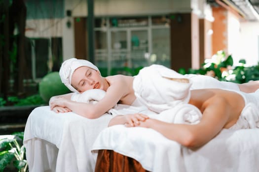 A portrait of a couple of a beautiful young caucasian woman with white towel rest on comfortable spa bed with relaxation while having body massage with professional masseur at spa salon.Tranquility.