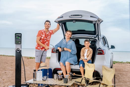 Family vacation trip traveling by the beach with electric car, happy family recharge EV car, enjoying outdoor camping coffee. Seascape travel and eco-friendly car for clean environment. Perpetual