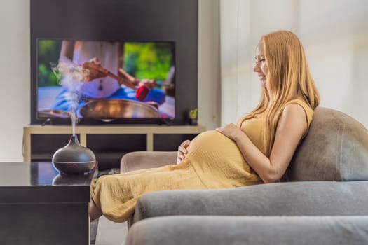 A blissful pregnant woman immerses in relaxation, savoring the soothing aroma from a diffuser while indulging in a calming TV video, embracing tranquility during her pregnant journey.