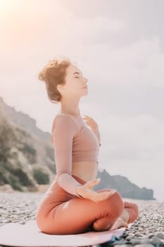 Young woman with long hair in white swimsuit and boho style braclets practicing outdoors on yoga mat by the sea on a sunset. Women's yoga fitness routine. Healthy lifestyle, harmony and meditation