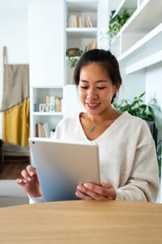 Vertical portrait of happy and smiling young Asian woman working at home office holding tablet reading document. Social media. Technology concept.