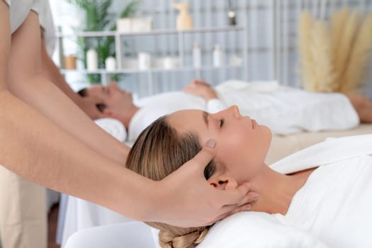 Caucasian couple enjoying relaxing anti-stress head massage and pampering facial beauty skin recreation leisure in dayspa modern light ambient at luxury resort or hotel spa salon. Quiescent