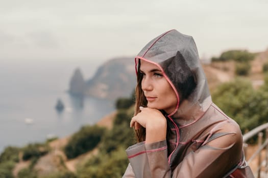 Woman rain park. Happy woman portrait wearing a raincoat with transparent umbrella outdoors on rainy day in park near sea. Girl on the nature on rainy overcast day