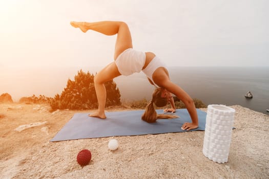 Middle aged well looking woman with black hair doing Pilates with the ring on the yoga mat near the sea on the pebble beach. Female fitness yoga concept. Healthy lifestyle, harmony and meditation.