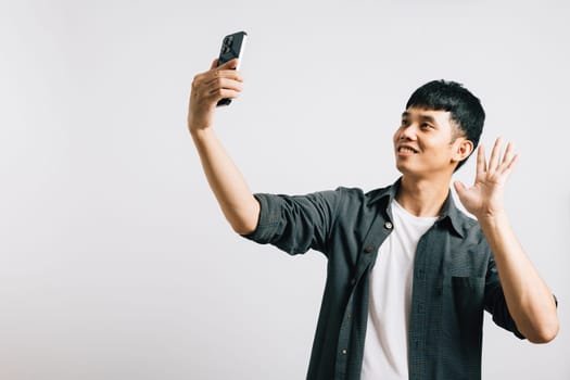 An excited Asian man smiles while making a selfie on his smartphone in a studio setting. Isolated on white, his joy is infectious. Say hello to self-expression