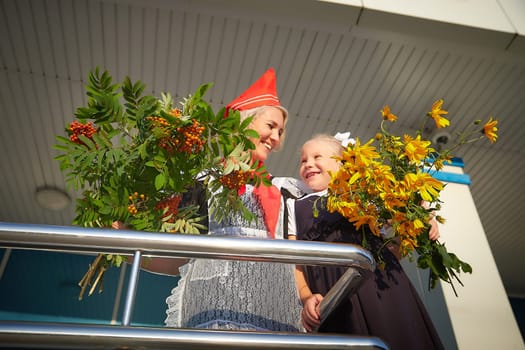 Young and adult schoolgirl on September 1 with flowers. Generations of schoolchildren of USSR and Russia. Female pioneer in red tie and October girl in modern uniform. Daughter and Mother having fun