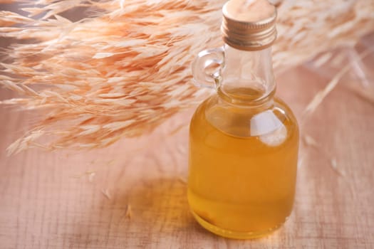 A clear bottle of golden oil rests by dried plants on wood.