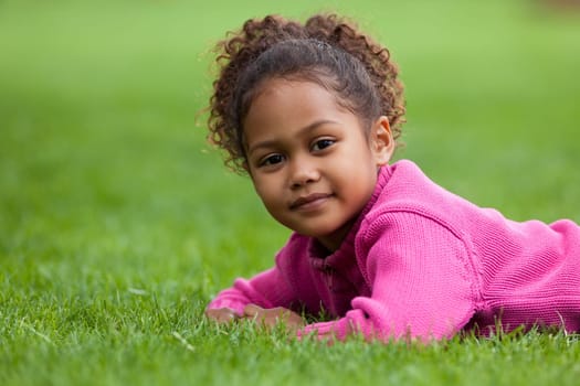 Outdoor portrait  of a cute little African Asian girl lying down on the grass