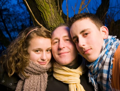 Portrait of a father with his two teenage teenagers in front of a tree at dusk