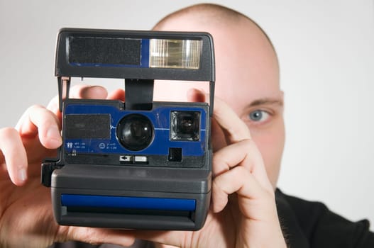 Head and shoulders shot of young man posing with instant camera against white background