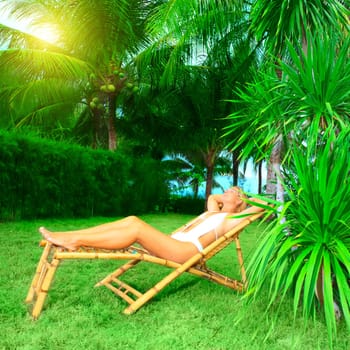 Young woman sunbathing on the chair in tropical garden