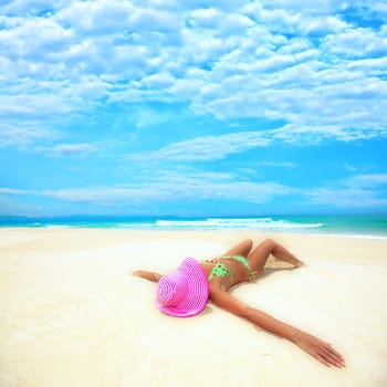 Woman in pink hat lies on the beach