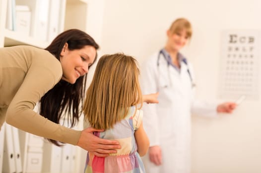 Female pediatrician pointing at eye chart mother and child visit
