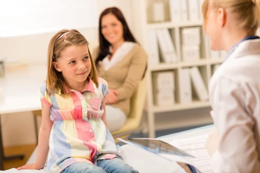 Little girl sitting on medical bed listening to pediatrician
