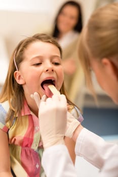 Little girl having throat examination with tongue depressor