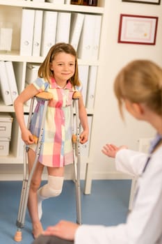 Little girl with bandaged leg standing with crutches surgery office