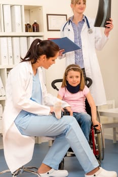 Little injured girl on wheelchair with doctors at medical office