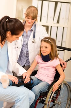 Little injured girl on wheelchair with doctors at medical office