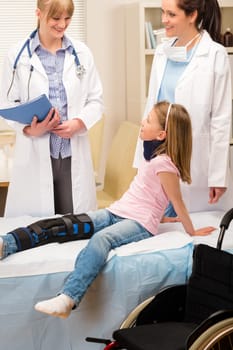Two female doctors examine broken leg little girl wheelchair