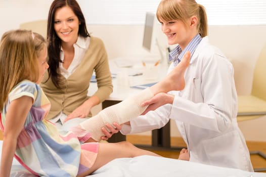 Female pediatrician checking broken bandaged leg of little girl