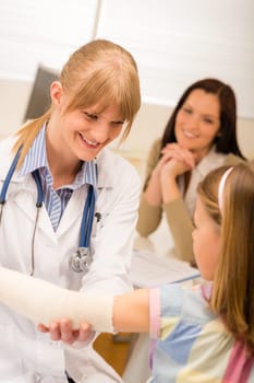 Female pediatrician checking bandage of girl broken arm