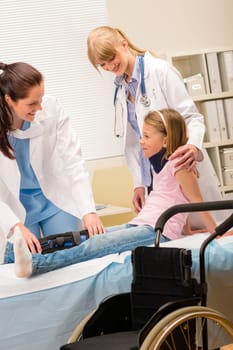 Two female doctors examine broken leg little girl wheelchair