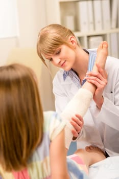 Female pediatrician checking broken bandaged leg of little girl