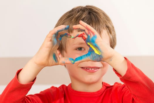 Boy paints with finger paints and forms a heart with his hands