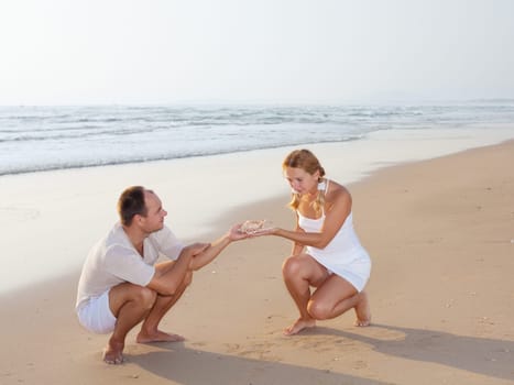 young couple with seashell on the tropical beach at sunrise time