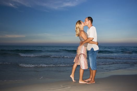 Young couple kissing near the ocean on sunset time