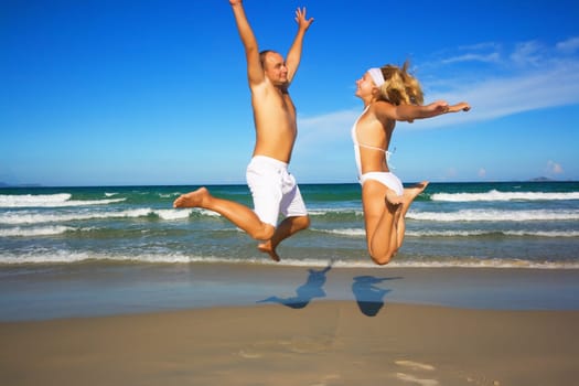 Young couple jumping on the tropical beach.