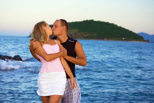 Young couple kissing near the ocean on sunset time