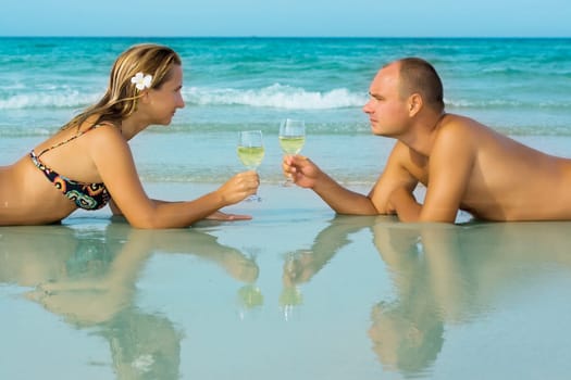 Young couple with glasses of white wine on the tropical beach