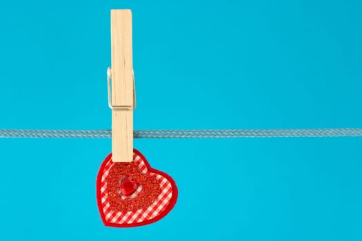 red decorative heart hung on clothesline. isolated on blue background