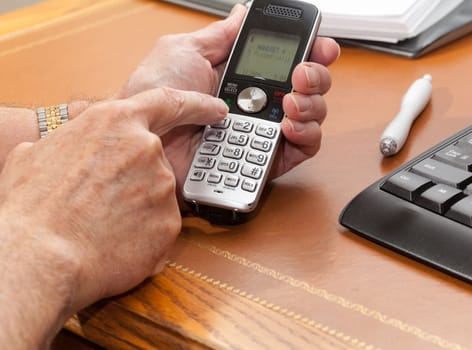 Caucasian man pressing buttons on wireless phone on leather desk