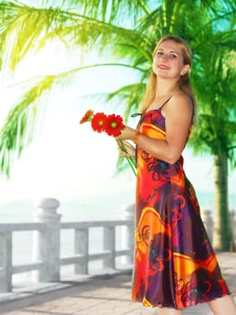 Young woman with gerbera flowers in red dress near the ocean