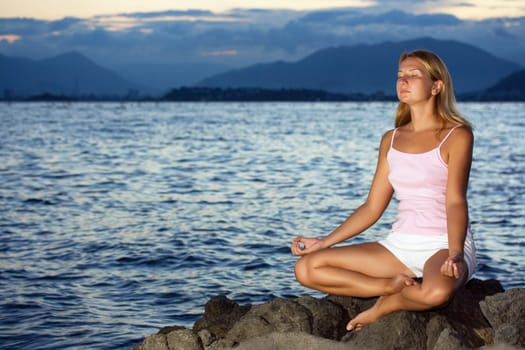 Young woman meditating at sunset time near ocean