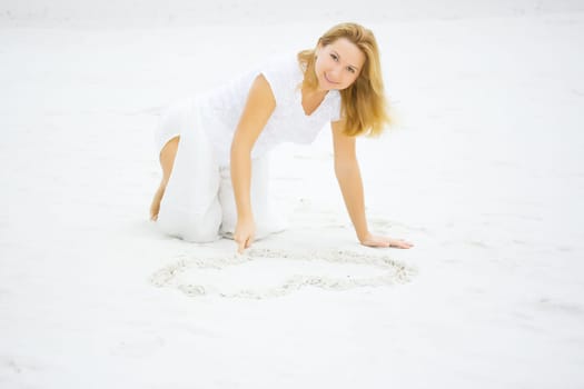 Young woman draws heart on white sand
