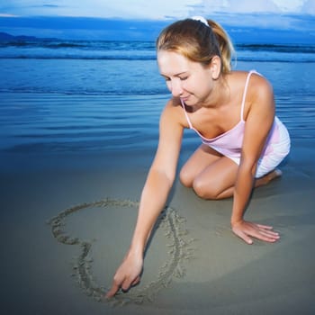 Young woman draws heart near the ocean on sunset time