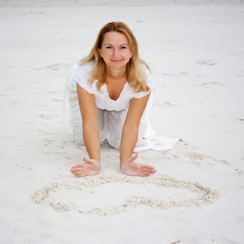 Young woman draws heart on white sand