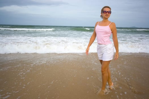 Young woman walking near ocean in sunglasses